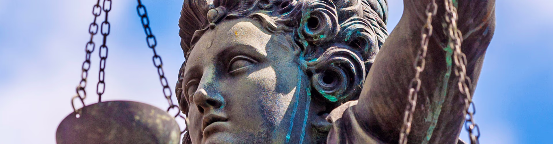 Close-up of a bronze Lady Justice statue holding scales against a blue sky.