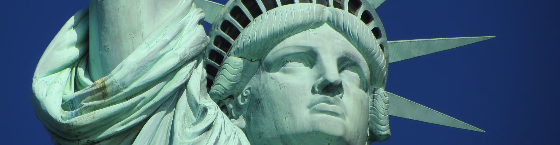 Close-up of the Statue of Liberty's face and crown against a deep blue sky.