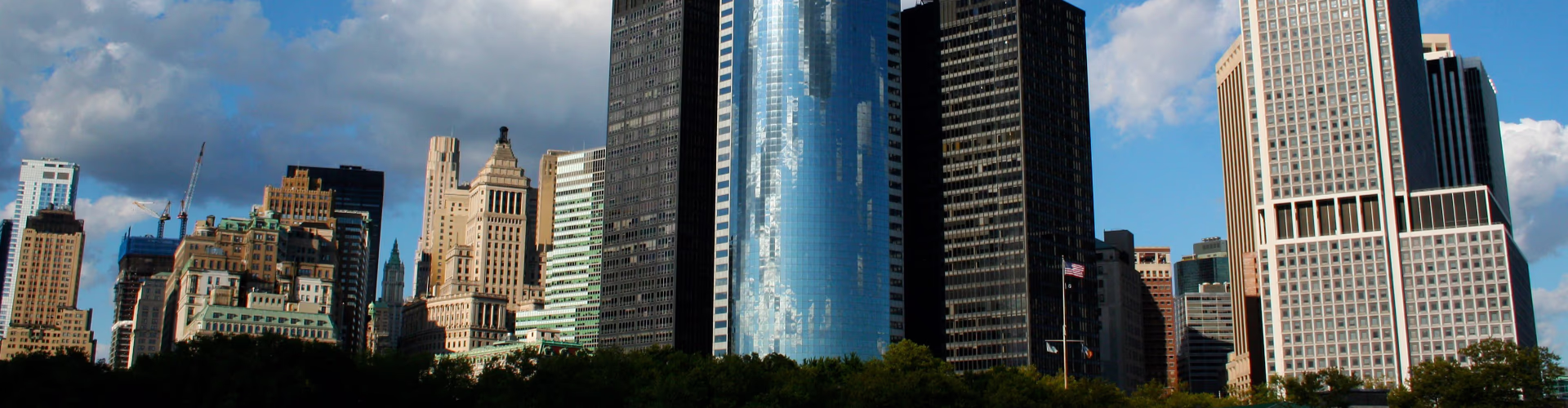 NYC skyline with skyscrapers and trees under a cloudy blue sky.